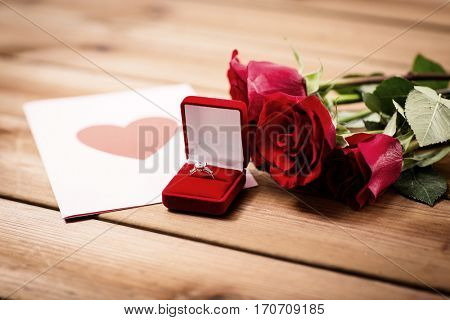 love, proposal, valentines day and holidays concept - close up of gift box with diamond engagement ring, red roses and greeting card on wood (vintage effect)