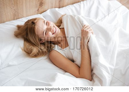 Top view of smiling woman lying on bed in bedroom