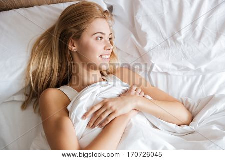 Top view of smiling woman lying on bed in bedroom and looking away