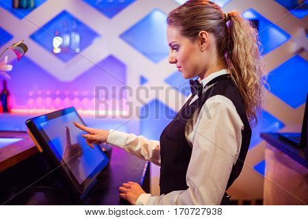 Side view of young barmaid using modern cash register at bar counter