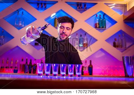 Bartender pouring alcohol in shot glasses on illuminated bar counter