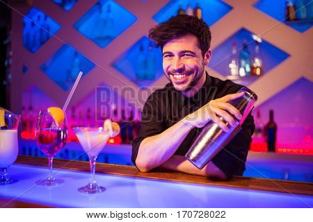 Portrait of bartender smiling while holding cocktail shaker at illuminated bar counter