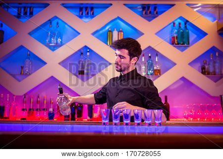Bartender pouring alcohol in shot glass at illuminated bar counter
