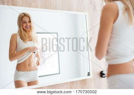 Smiling Woman looking at himself near the mirror and showing stomach
