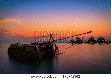 The old fishing boat capsized on sea at sunset in Phuket Thailand.