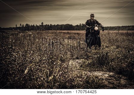 Young, stylish man on vintage custom racer in field.