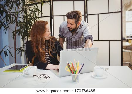 Happy young colleagues dicussing while using laptop at creative office