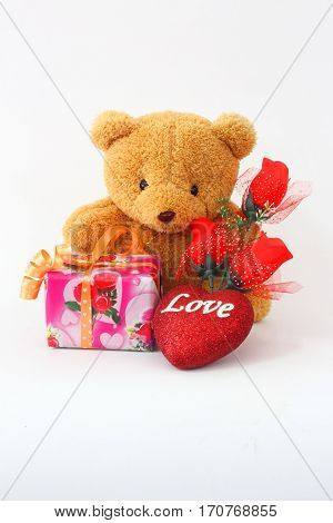 Brown teddy bear with a red rose and a gift box on a white background.