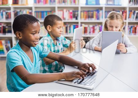 Kids using laptop and digital tablet in library at school