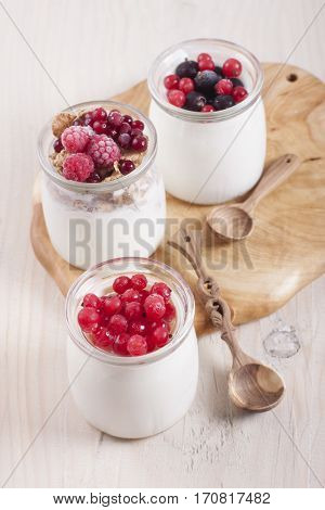 Homemade yogurt with frozen berries red currants black currants raspberries and cranberries in three banks