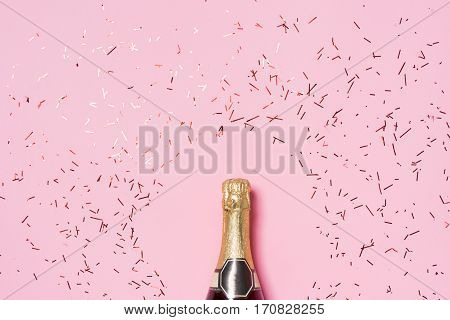 Flat lay of Celebration. Champagne bottle with colorful party streamers on pink background.