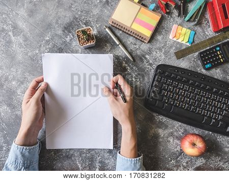 Top view of Male hands holding paper sheet with Office supplies on Grunge gray background