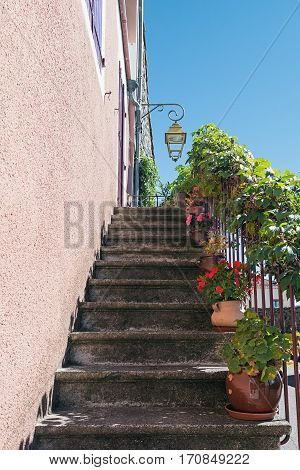 Old staircase in front of the door decorated with plants in flower pots in the picturesque village of Mirabel Ardèche, France.