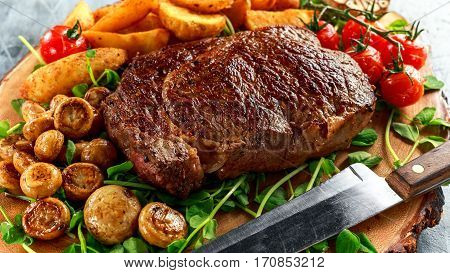 Cooked Beef Ribeye Steak with Potato, Mushrooms, tomatoes on wooden board