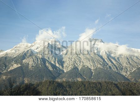 Austria - January, 2017 For forest seen huge mountain peaks, mountain ranges stretch under the sky, the snow on the tops of the mountains, the clouds in the sky, alpine mountains against the blue sky