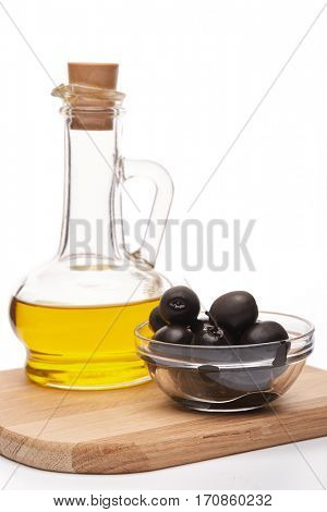 Glass cruet with Extra virgin olive oil, canned black olives in bowl stand on a wooden cutting board on a white background.