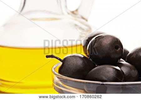 Glass cruet with Extra virgin olive oil, canned black olives in bowl stand on a wooden cutting board on a white background.