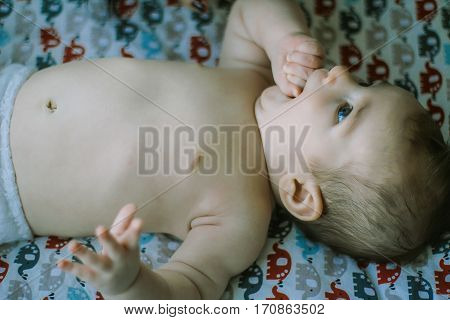 little baby lying on the bed in the diaper. thumb-sucking