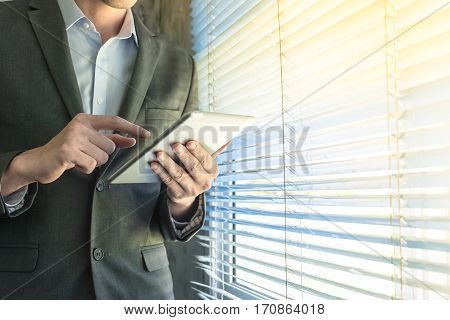 Close up of businessman using tablet device while standing at a window in an office