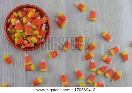 Candy Corn in Orange Bowl with Mess Spill Over across gray background