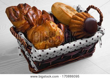 Assortment of fresh pastries buns bread - large loaf Pie with poppy seeds buns with candied fruit cupcake bun with chocolate in special wicker basket for pastries bread. White wooden background.