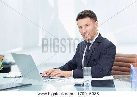 businessman in black business suit sitting behind a Desk in the spacious office and working on laptop keyboard