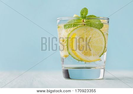 Mineral infused water with limes, lemons, ice and mint leaves on blue background. Homemade detox soda recipe.