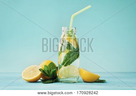 Lemonade drink of soda water lemon and mint leaves in jar on turquoise background.