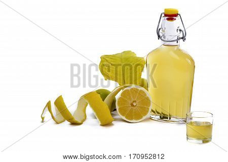 Open glass decanter bottle and shot glass filled with yellow lemon liquor or limoncello or limoncino on white. Peeled natural organic lemon.