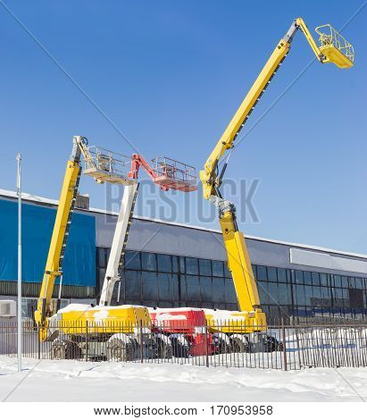 The three different self propelled wheeled hydraulic articulated boom lift with telescoping booms and baskets against the sky and the industrial building in winter sunny day