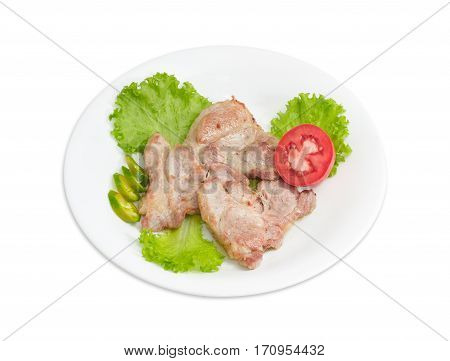 Several slices of fried pork neck on lettuce leaves sliced green chili and half of tomato on white dish on a light background
