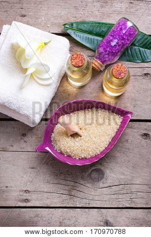 Spa setting. Sea salt in bowl in form of leaf with towels and bottles with oil on vintage wooden background. Selective focus. Verical image.