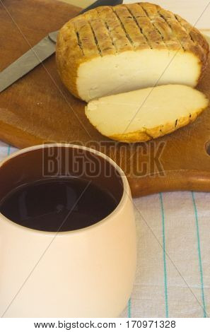 cut head of traditional Adygei cheese handmade with knife and a Cup of coffee on wooden Board