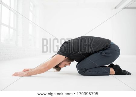 Handsome man in the black sportswear doing yoga in the white gym interior