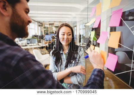 Female photo editor standing near male coworker writing on sticky note in meeting room