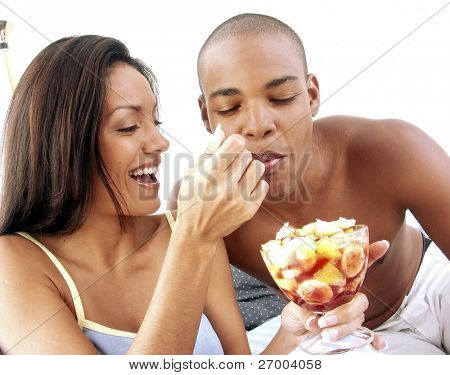 Unge hispanic par nyder og spise frugtsalat på sengen.