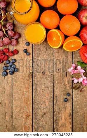 Orange Juice, Fresh Oranges, Apples, Grapes, Raspberries, Blueberries And Spring Flowers On A Wooden