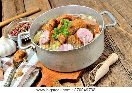 Garlic Soup In An Old Saucepan With Sausage, Fresh Garlic Bulbs, Cloves, Colored Pepper, Wooden Spoo