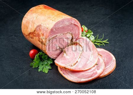 Traditional Allgauer veal roast roll sausage sliced and as piece with tomatoes and chili as closeup on a slate slab
