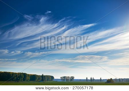 beautiful sky, field and forest in far in autumn season, bright sunlight and cirrus clouds