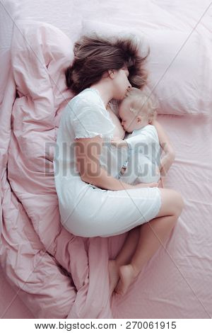 A Young Mother Breastfeeds Her Baby Lying In A Pink Bed. Hugs His. Sleeping