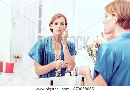 Calm Short-haired Young Gender-queer Applying Full Coverage Foundation