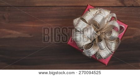 One Classic Red Gift Box Golden Bow On Natural Wood Background, Soft Blur Focus At The Left Area For