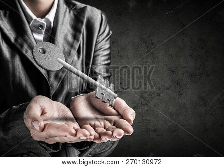 Cropped Image Of Businessman In Suit Keeping Stone Key Symbol In Hands With Dark Wall On Background.