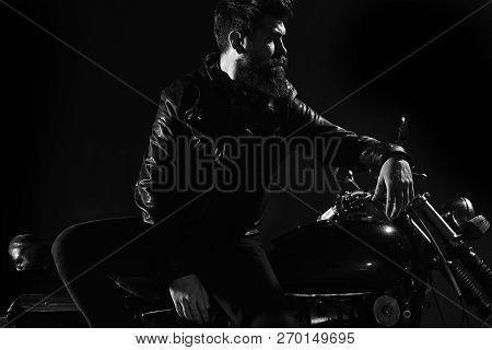 Brutality And Masculine Concept. Man With Beard, Biker In Leather Jacket Lean On Motor Bike In Darkn