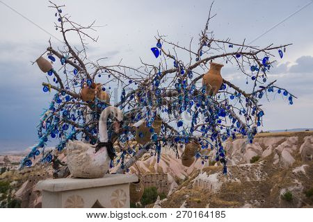 White Toy Swan Near The Tree Of Desires. Evil Eye In Tree Behind Uchisar Castle In Cappadocia, Turke