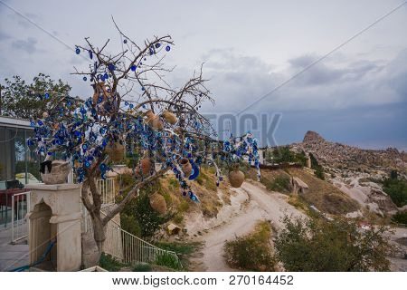 White Toy Swan Near The Tree Of Desires. Evil Eye In Tree Behind Uchisar Castle In Cappadocia, Turke