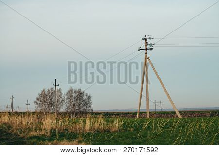Atmospheric Landscape With Power Lines In Green Field With Dirt Road On Background Of Trees Under Bl