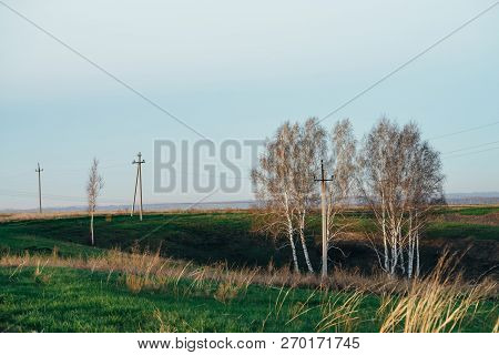 Atmospheric Landscape With Power Lines In Green Field With Road And Trees Under Blue Sky. Background