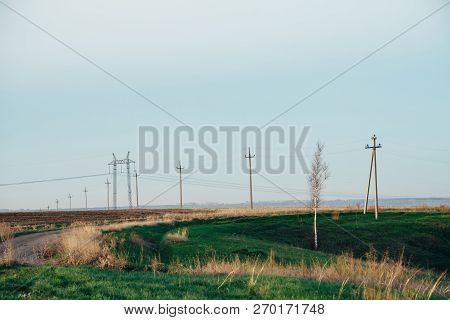 Atmospheric Landscape With Power Lines In Green Field With Road And Tree Under Blue Sky. Background 